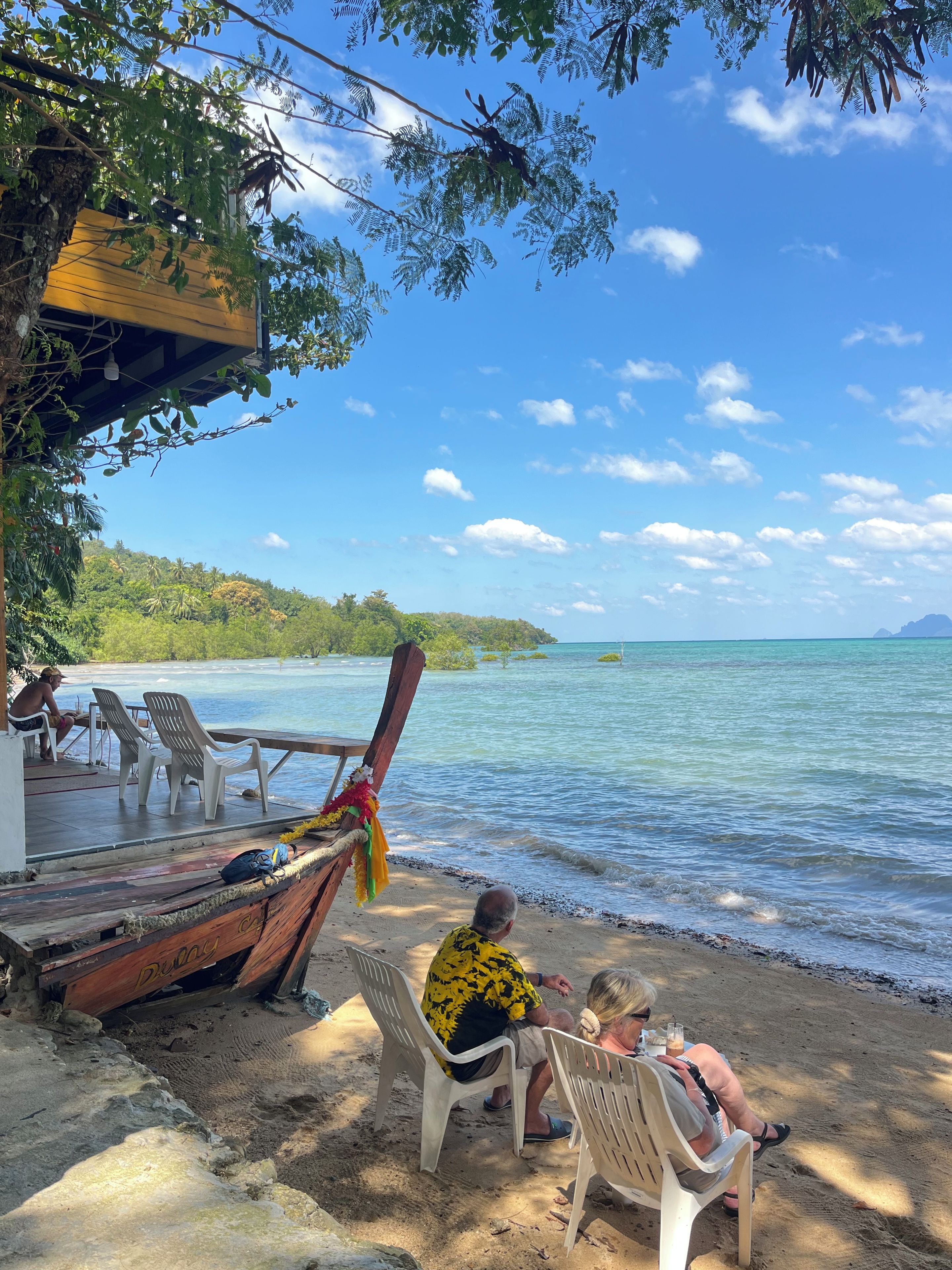 A beachside setting with a wooden deck, plastic chairs, and a view of the sea.