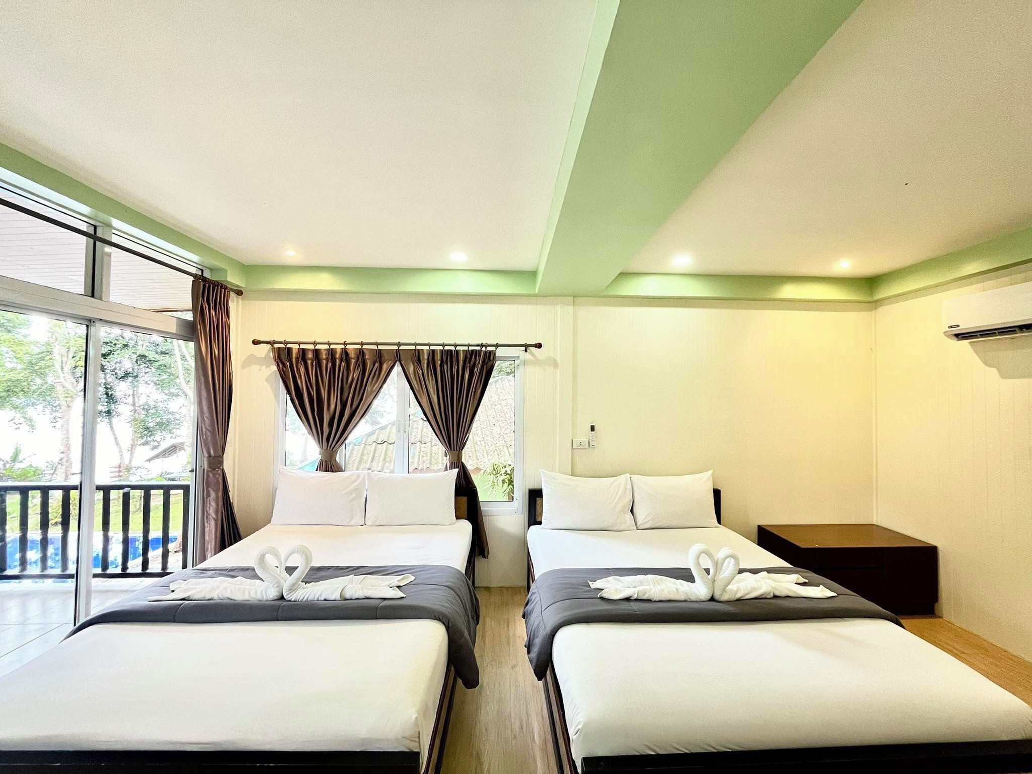A hotel room with two beds, a balcony, and a view of trees.