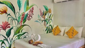 Een hotelkamer met een bed, een wanddecoratie van tropische planten en een airconditioningsunit.