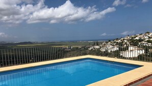 A rectangular pool with a tiled edge, surrounded by a metal fence, overlooking a coastal village with houses and a clear sky. - El Valle Verde - Perfect Family Retreat (Monte Pego)