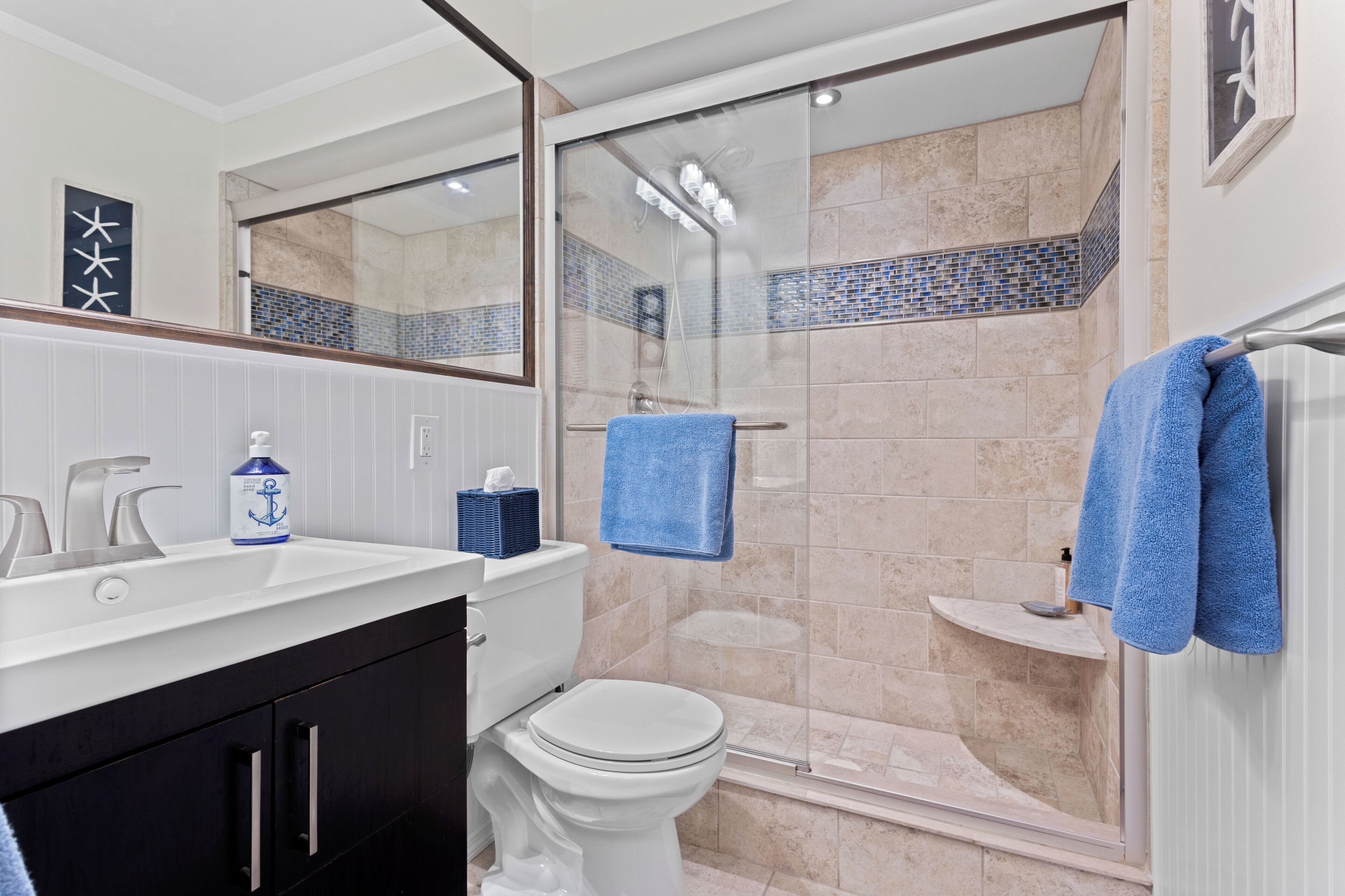 A bathroom with a white sink, a toilet, a glass-enclosed shower, and a blue towel hanging on a rack.