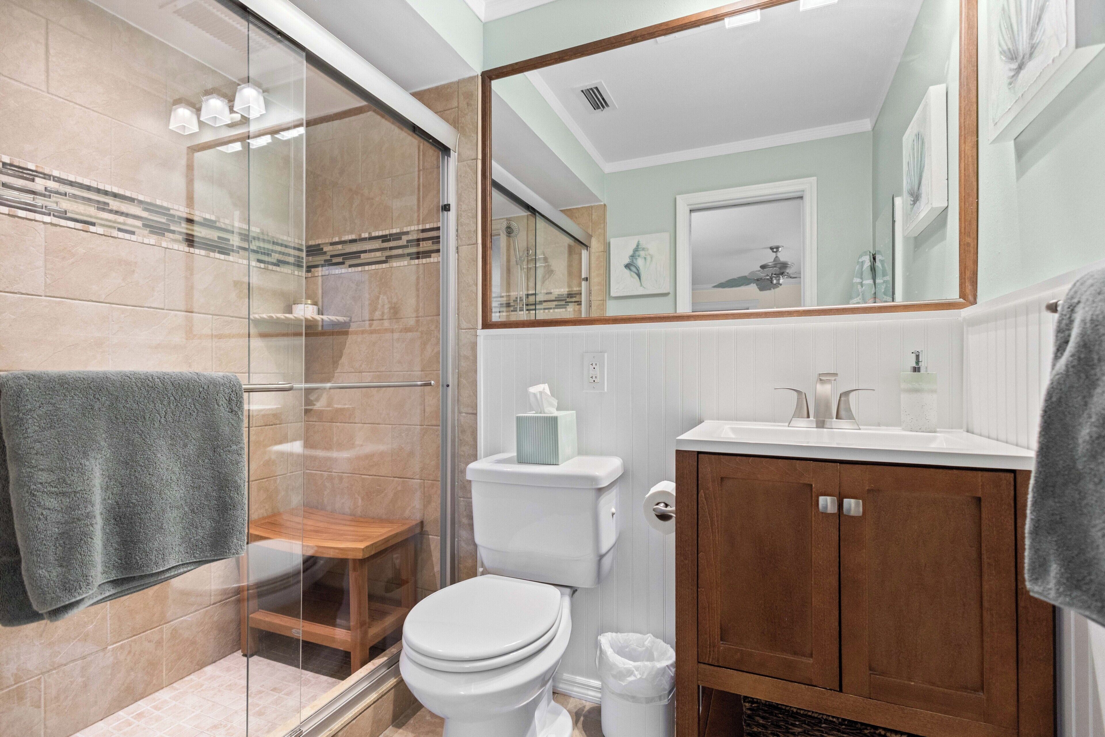 A bathroom with a glass shower enclosure, a toilet, a sink with a mirror, and wooden cabinets.