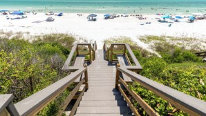Een houten trap die naar een strand leidt met parasols en strandstoelen.