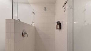 A modern bathroom with white tiles, a glass shower enclosure, and a wall-mounted soap dispenser.