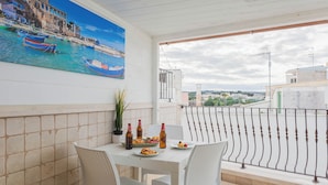 A balcony with a table set for two, a potted plant, and a painting of a coastal scene. - Polly House by Wonderful Italy (Polignano a Mare)