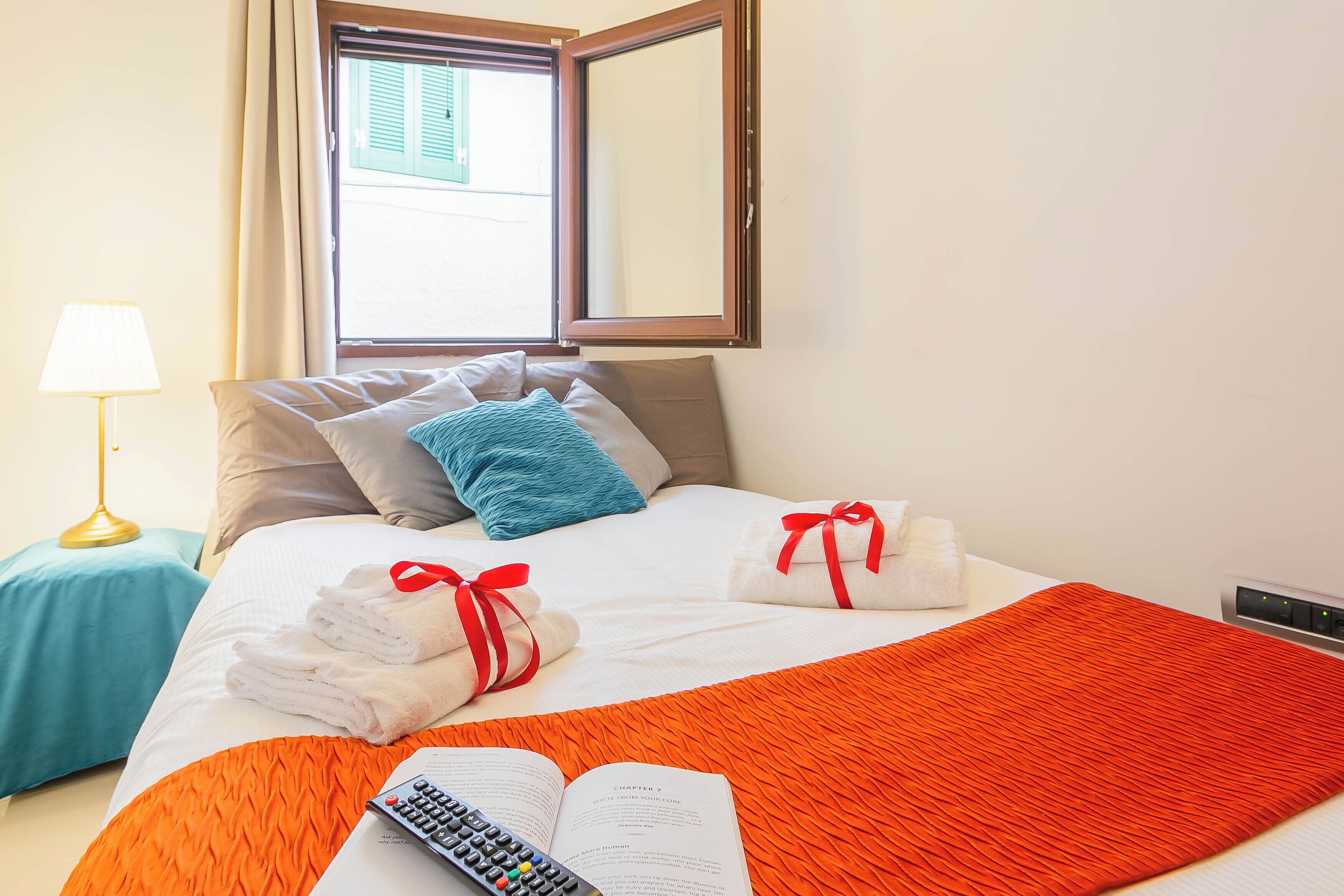 A hotel room with a bed, a book, a remote control, and towels.