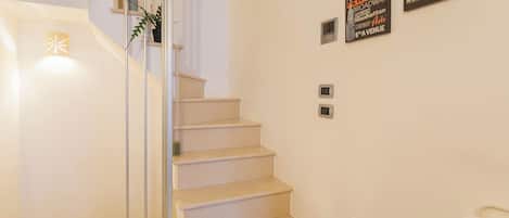 Una escalera con barandilla de vidrio, una planta en maceta y letreros en la pared que anuncian lugares de Nueva York.