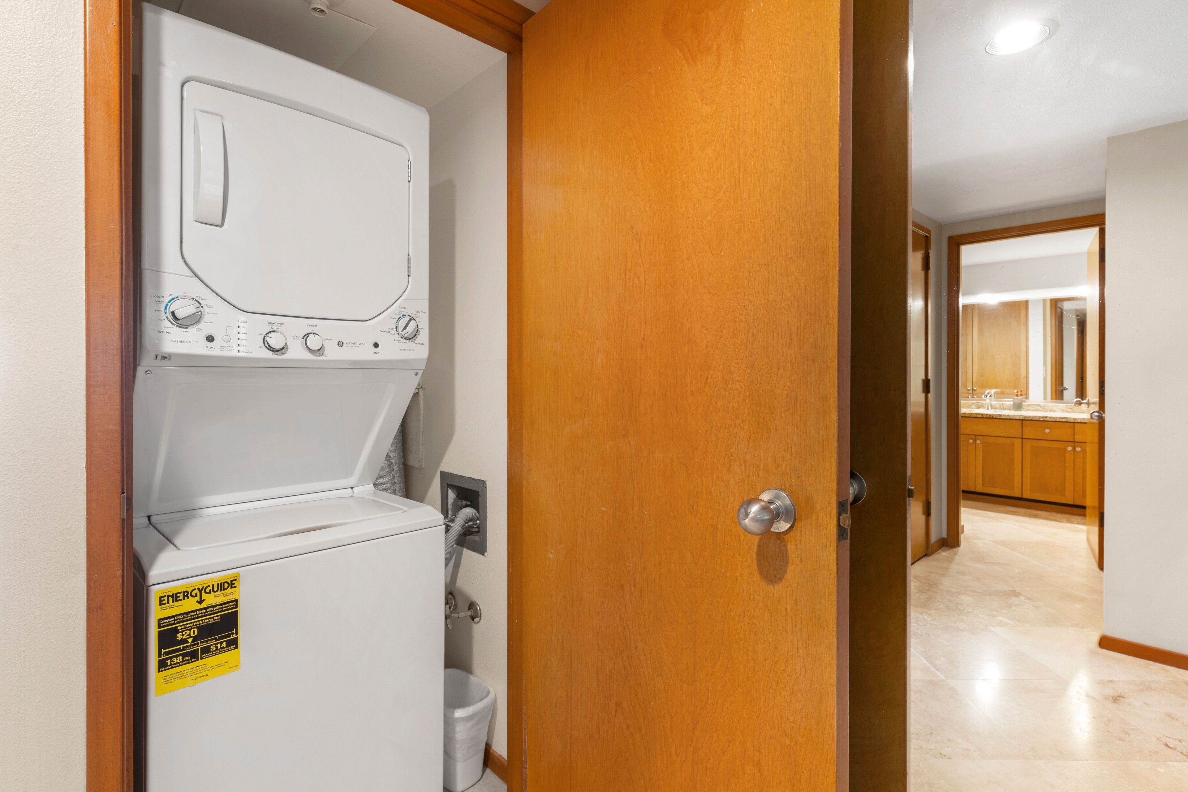 A laundry room with a front-loading washer and dryer, a yellow energy efficiency sticker, and a door leading to a bathroom.