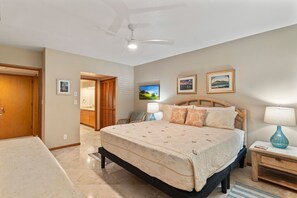 A bedroom with a bed, a nightstand, a lamp, a ceiling fan, and a door leading to another room. - Makena Surf, #g-103 2 Bedroom Condo by RedAwning (Kihei)