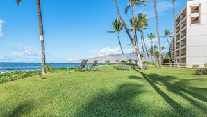 A resort with a grassy lawn, palm trees, lounge chairs, and a view of the ocean. - Sugar Beach Resort, #235 1 Bedroom Condo by RedAwning (Kihei)