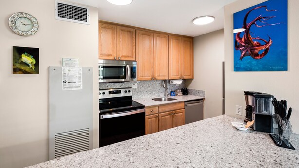 A modern kitchen with granite countertops, stainless steel appliances, wooden cabinets, and a wall-mounted clock. - Sugar Beach Resort, #409 1 Bedroom Condo by RedAwning (Kihei)