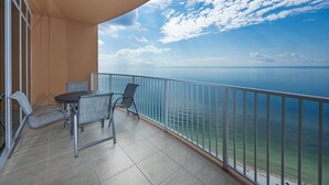 A balcony with a view of the sea, a table, and two chairs.