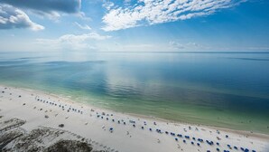 A beach with clear turquoise water, white sand, and blue umbrellas.