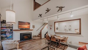 Ein geräumiges Wohnzimmer mit Kamin, Fernseher und Essbereich mit Holzzmöbeln.