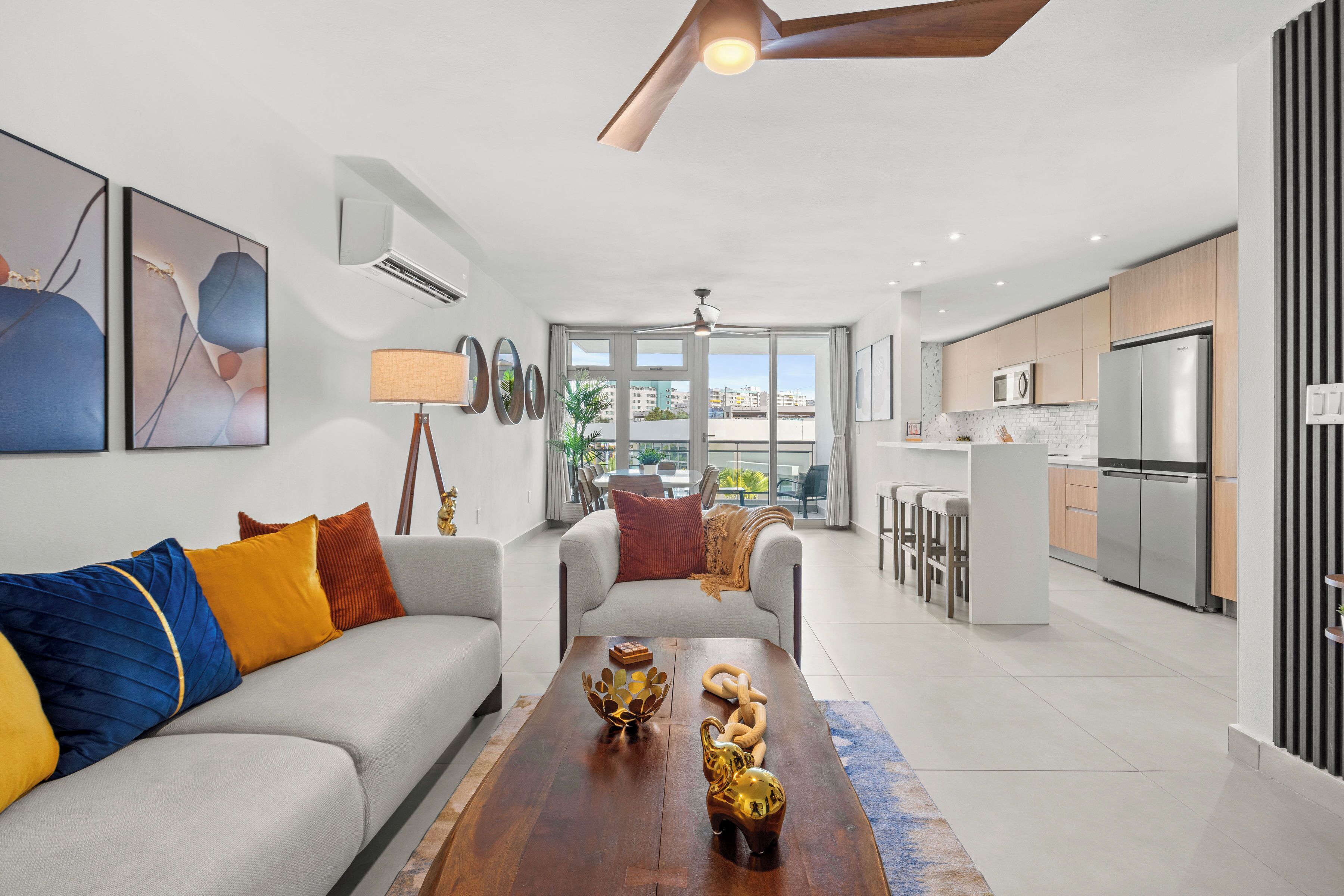 Una sala moderna con sofá, una mesa de centro y elementos decorativos. Incluye una zona de cocina con electrodomésticos y una zona de comedor con mesa y sillas.