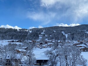 Un village enneigé, avec des maisons en bois, une piste de ski et une montagne boisée en arrière-plan.