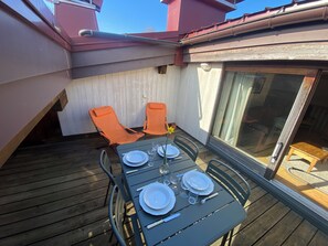 A covered outdoor dining area with a table set for four, two orange chairs, and a sliding glass door leading to an interior space.