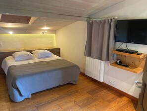 A hotel room with a bed, a TV on a wooden shelf, a radiator, and a window with curtains.
