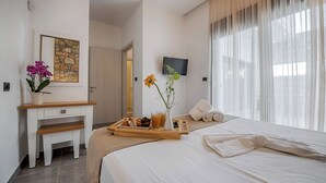 Quarto de hotel com cama, escrivaninha com bandeja de café da manhã, televisão e janela com cortinas.