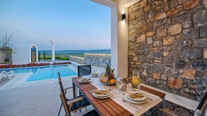 Un espace repas avec vue sur la piscine, un mur en pierre et des sièges d’extérieur.