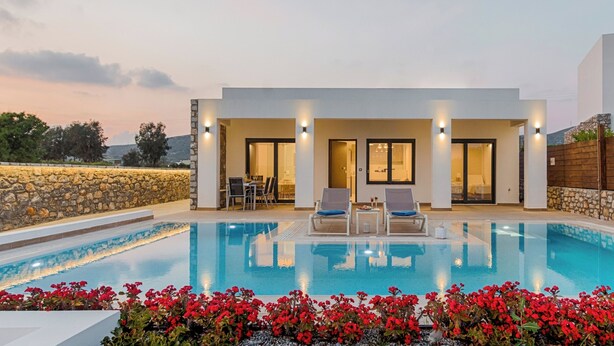 Un espace moderne aménagé au bord de la piscine, avec une piscine à eau claire, deux chaises longues et un mur en pierre.