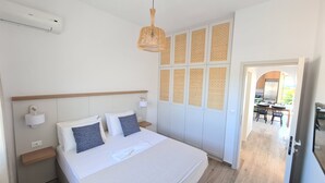 Un dormitorio con cama, mesitas de noche, lámpara colgante, armario con puertas estampadas y un acceso abierto a un comedor.