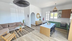 Una sala de estar moderna con un sofá, una mesa de centro y un comedor con sillas. La cocina tiene gabinetes verdes y una estufa.