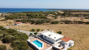 Una villa moderna con piscina, rodeada de pastizal seco y vistas al mar.