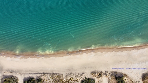 Vista aérea de una playa con agua turquesa cristalina y una orilla arenosa.