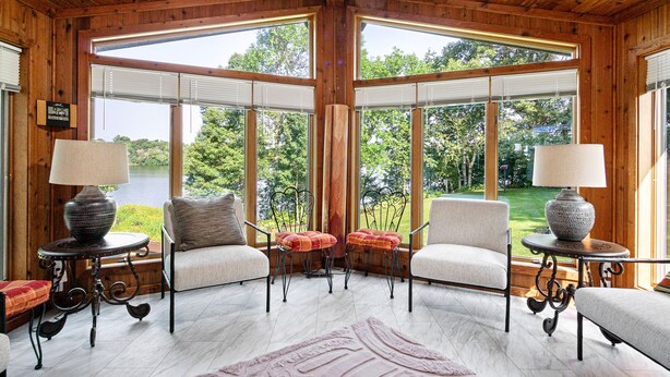 A wooden interior with large windows, two armchairs, a table, and a lamp. - Lake Wissota Lookout – A Luxury Escape (Chippewa Falls)
