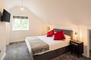 Une chambre à coucher avec un lit, un téléviseur fixé au mur, une fenêtre donnant sur un paysage verdoyant et une lampe de chevet.