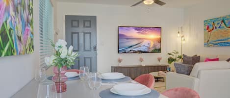 A dining area with a table set for four, a ceiling fan, and a painting of a sunset.