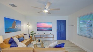 Una sala de estar con un sofá color beige, una mesa de centro de vidrio y un ventilador de techo.
