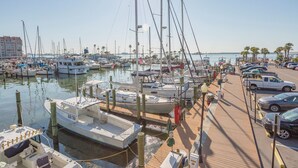 Un puerto deportivo con varias embarcaciones amarradas, un paseo marítimo de madera y un aparcamiento con coches.