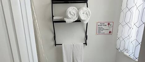 A small bathroom with a toilet, a towel rack with two towels, a sign prohibiting flushing of certain items, and a patterned shower curtain.
