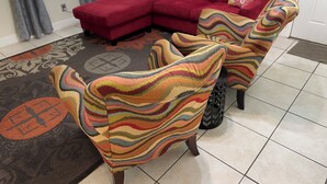 A living room with a red sectional sofa, colorful armchairs, and a patterned rug. - Cozy 3-bedroom house in gorgeous Fort Walton Beach with WiFi, AC all amenities  (Fort Walton Beach)