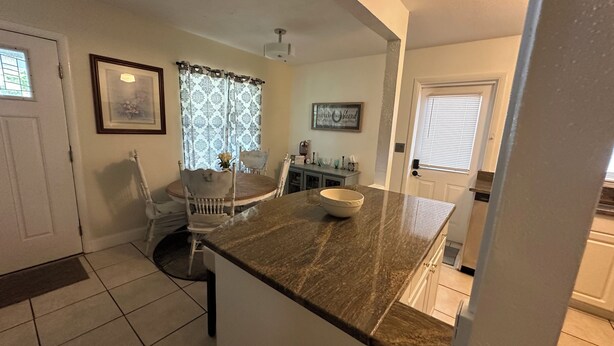A kitchen with a marble countertop, a dining table with chairs, and a window with patterned curtains. - Cozy 3-bedroom house in gorgeous Fort Walton Beach with WiFi, AC all amenities  (Fort Walton Beach)