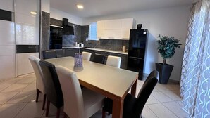 A modern kitchen with dark countertops, a black refrigerator, and a dining area with a table and chairs. - Apartments Lucija & Andora (Kastela)