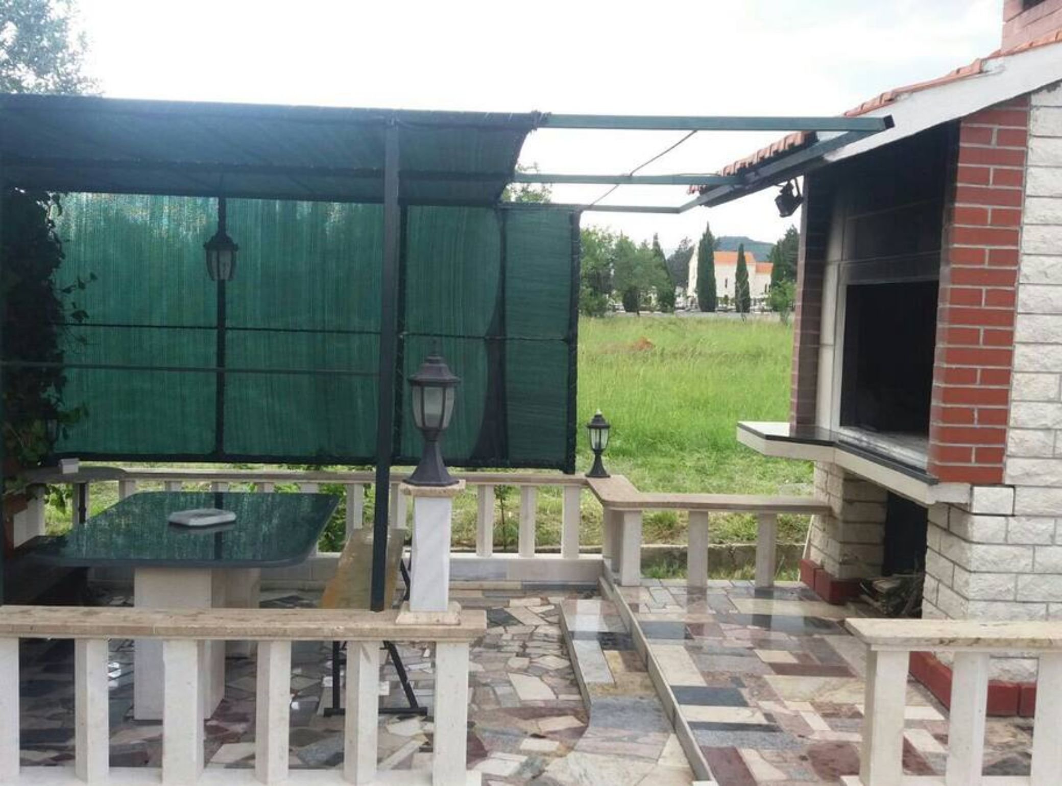 An outdoor patio area with a covered seating area, a barbecue grill, and a view of a grassy field.