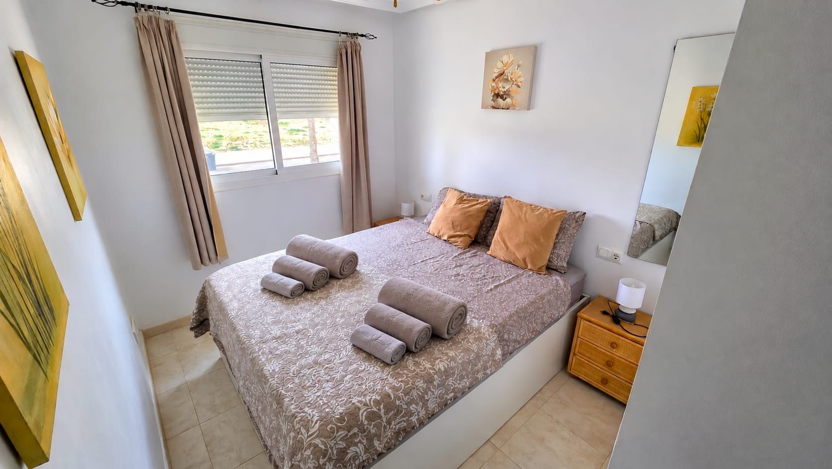 Un dormitorio con cama, almohadas, mesita de noche, lámpara y obras de arte en las paredes.