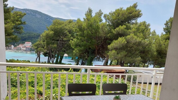 A balcony with a table and chairs, overlooking a coastal area with trees and buildings. - Beach House Žuljana (Ston)