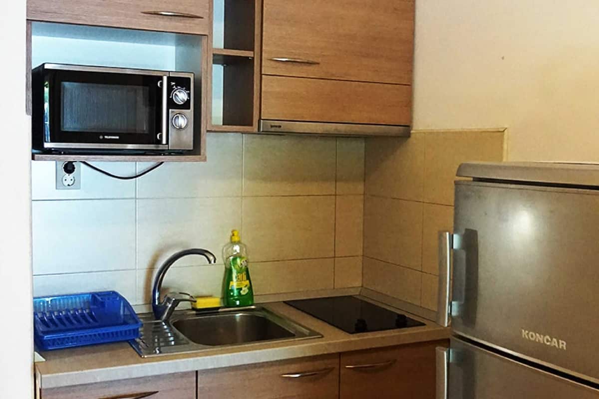 A compact kitchen with wooden cabinets, a built-in microwave, a stainless steel sink, and a Koncar refrigerator.