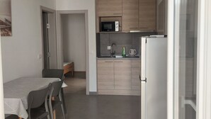 A compact kitchen with a microwave, kettle, and a refrigerator. There is a dining area with a table and chairs. - Beach House Žuljana (Ston)