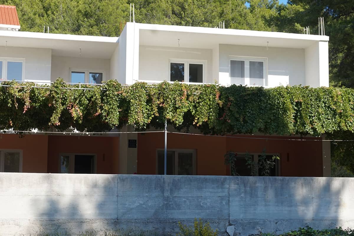 A modern building with a white facade and a lower section covered in green ivy.