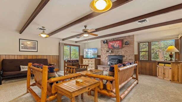 A cozy living room with a wooden coffee table, a sofa, and a fireplace. There are two ceiling fans and a TV mounted on the wall.