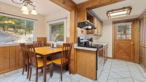 A wooden interior with a dining table, chairs, a kitchen area, and a view of the outdoors.
