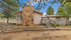A rustic cabin with a stone chimney, wooden exterior, and a small porch.