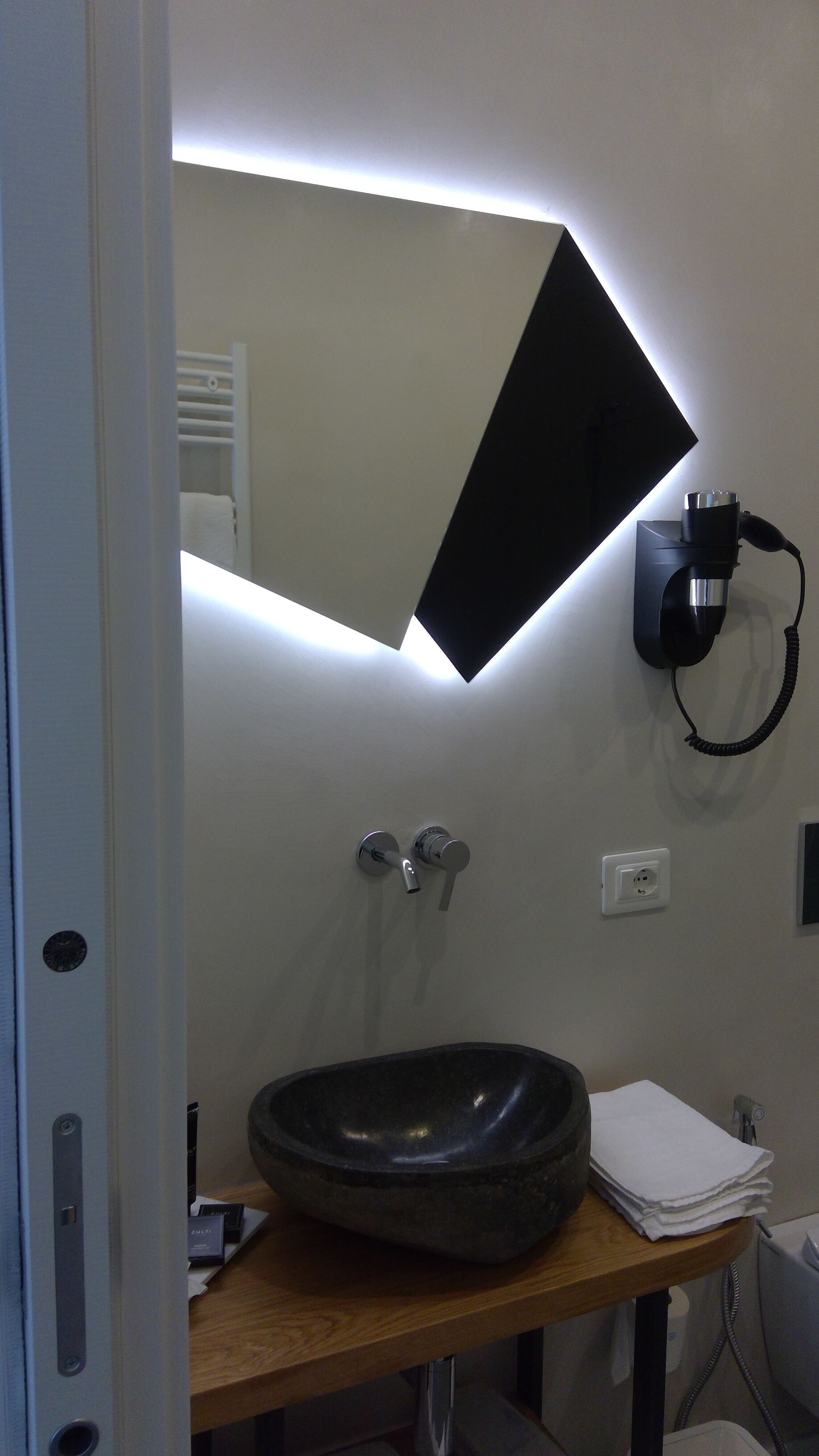 A bathroom with a modern sink, a mirror, and a wall-mounted hairdryer.