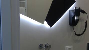 A bathroom with a modern sink, a mirror, and a wall-mounted hairdryer.