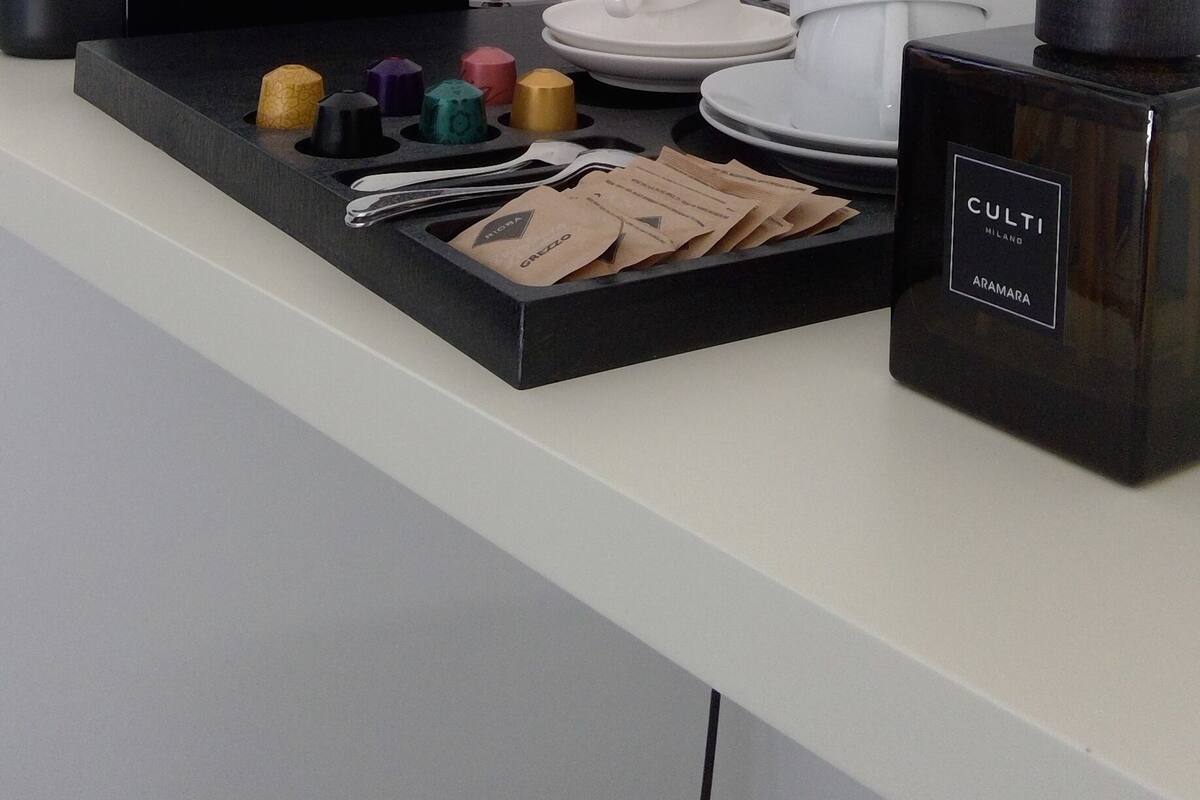 Minibar de una habitación de hotel con cafetera, bolsitas de té y un candelabro.
